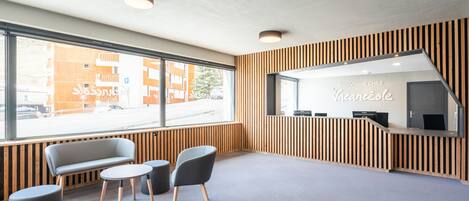 A reception area with a wooden panel wall, a reception desk, a seating area with a bench and two chairs, and a large window offering a view of the street.