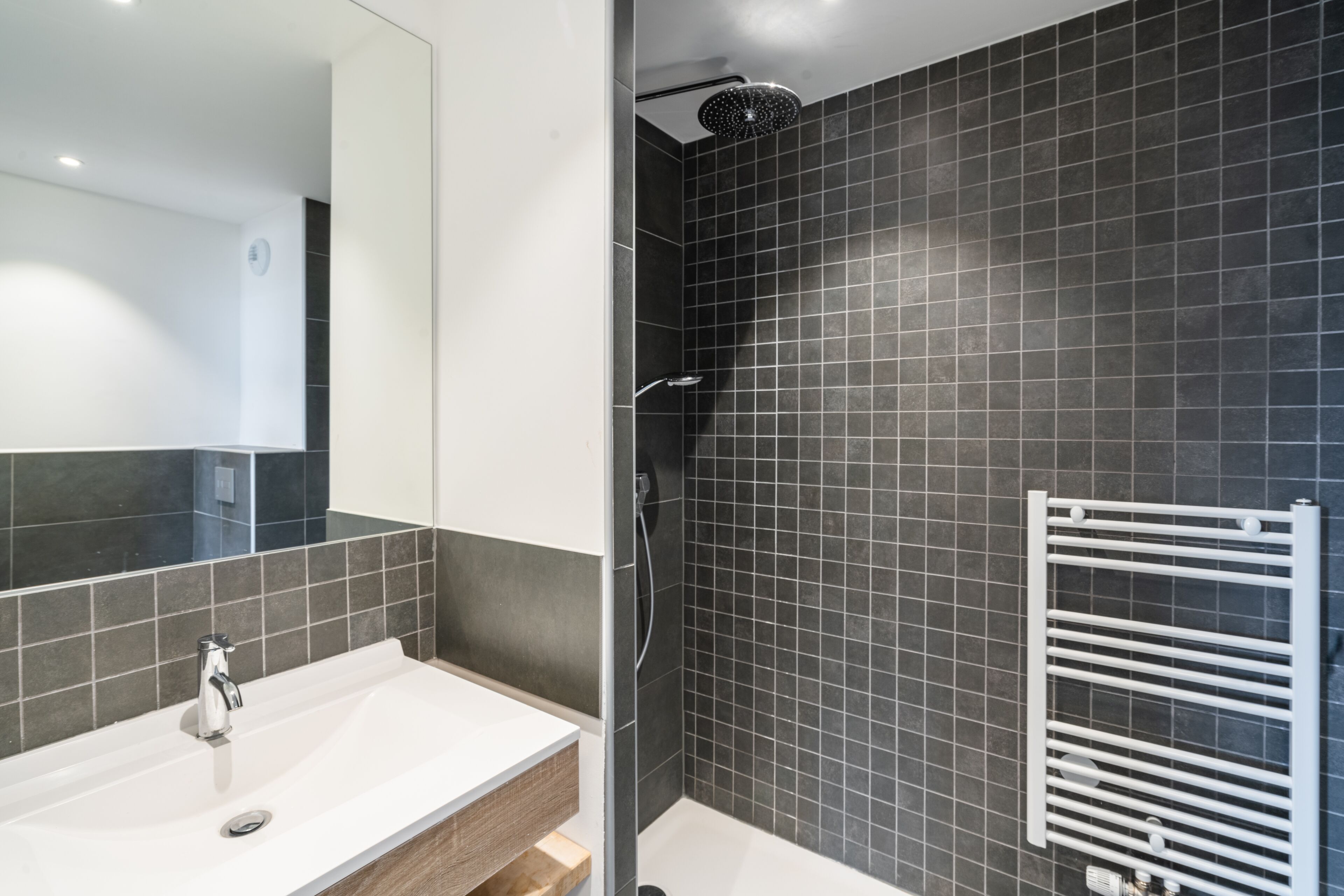 A modern bathroom with a white sink, dark tiled walls, and a glass-enclosed shower area.