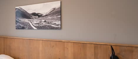 A bedroom with two beds, a wooden headboard, a bedside table, and a wall-mounted lamp.
