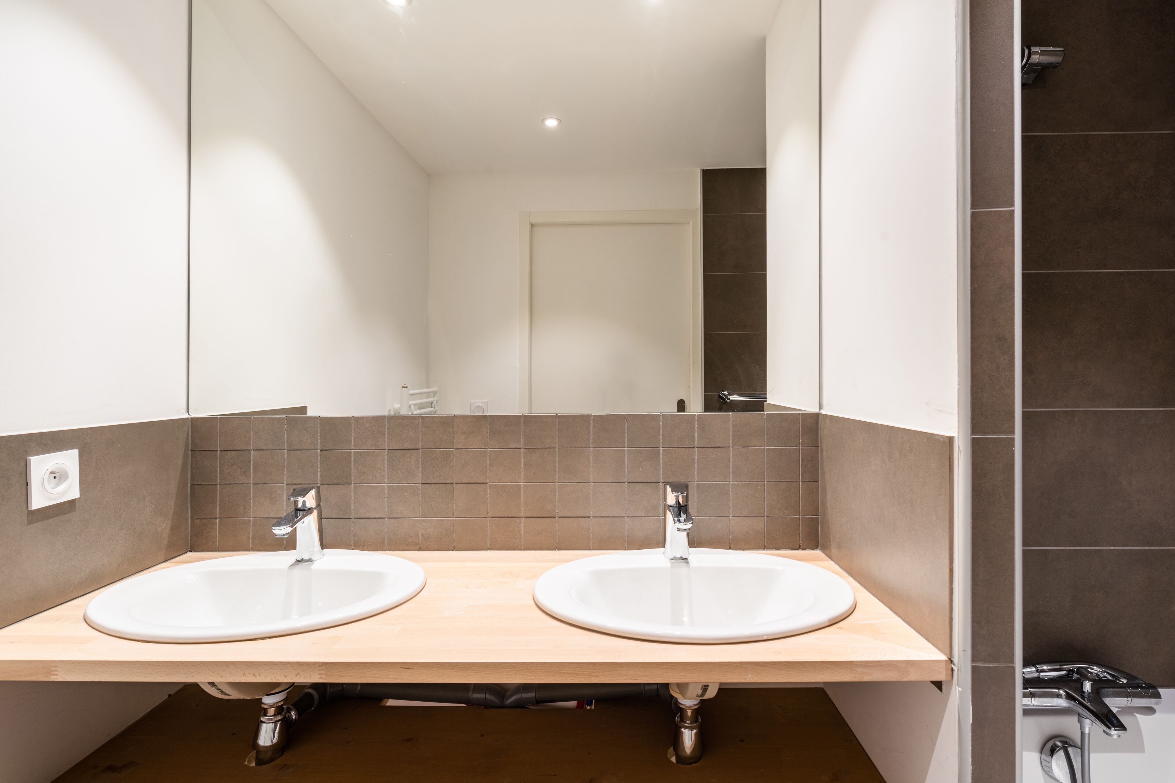 Un baño moderno con dos lavamanos, un espejo y una zona de ducha.