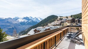 Un balcon en bois offrant une vue sur des montagnes enneigées et un village situé en contrebas.
