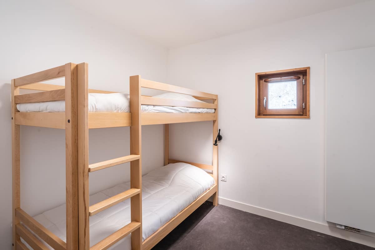 Une chambre avec un lit superposé, une petite fenêtre et une porte.