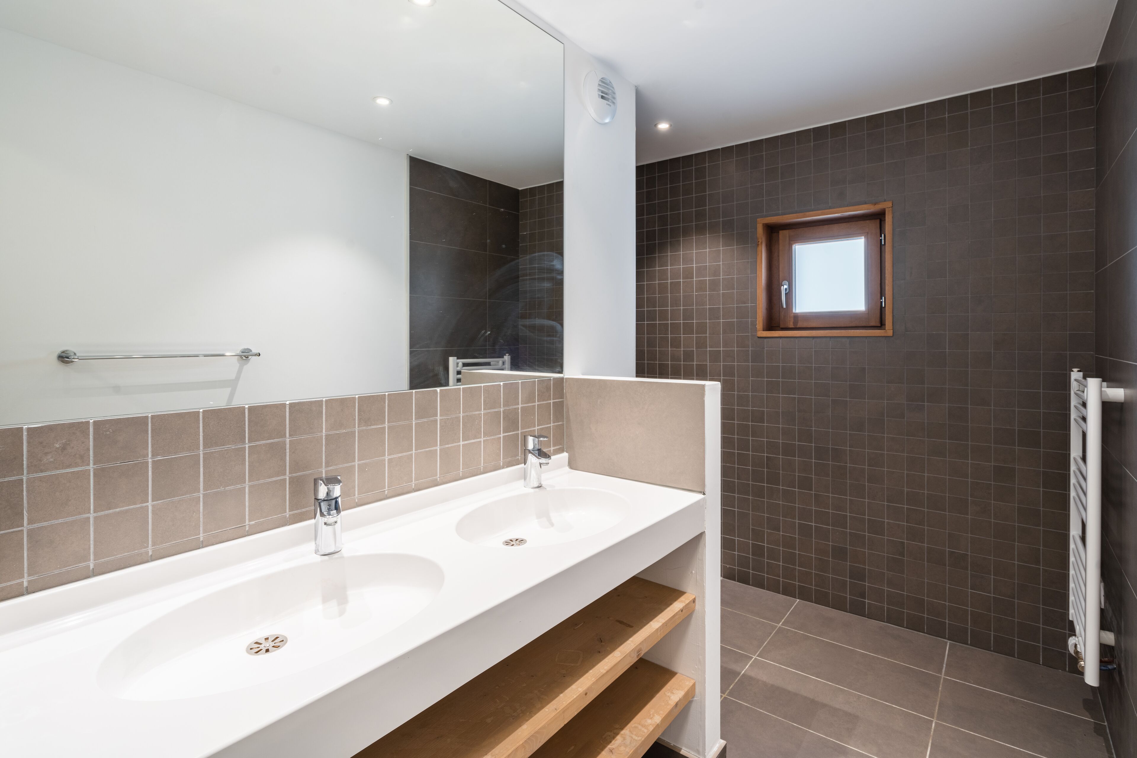 A modern bathroom with two sinks, a large mirror, and a shower area.