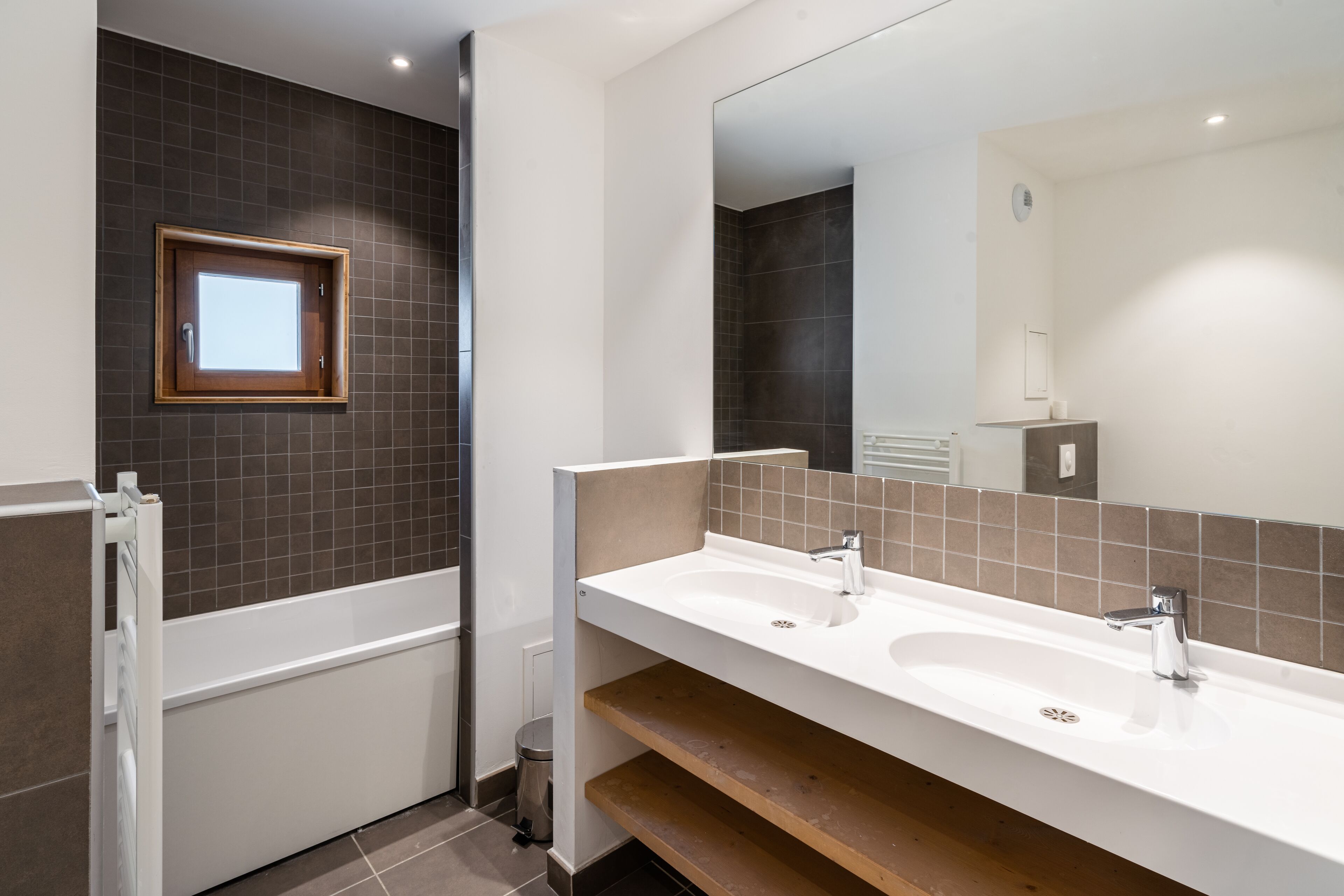 Un baño moderno con dos lavamanos, un espejo grande y una ventana.