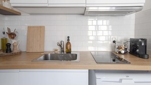 Une cuisine moderne avec des meubles blancs, un évier en acier inoxydable, une planche à découper en bois, une machine à café et une bouilloire.