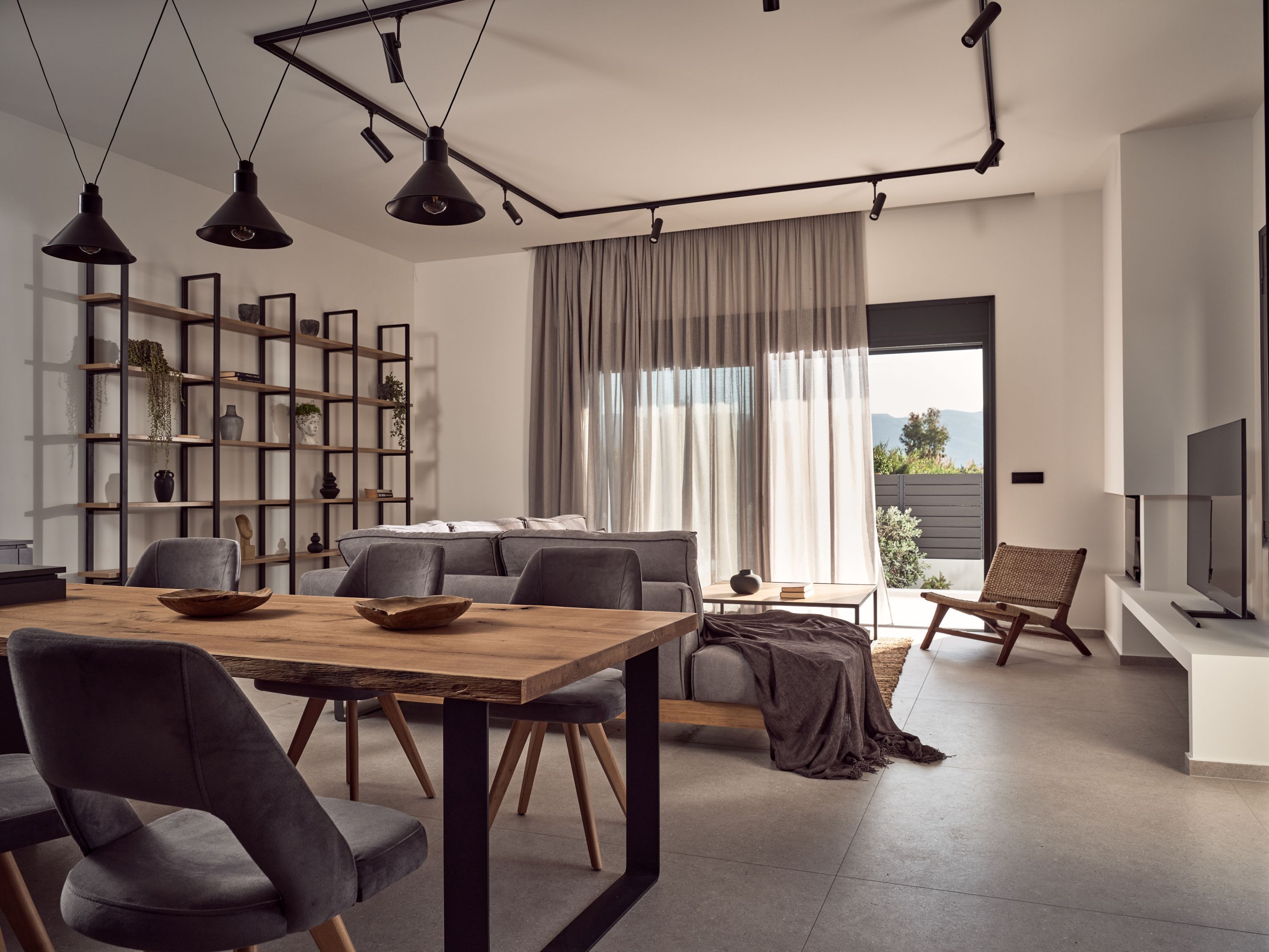 Ein modernes Wohnzimmer mit einem Holzesstisch, grauen Sofas und einem Bücherregal.