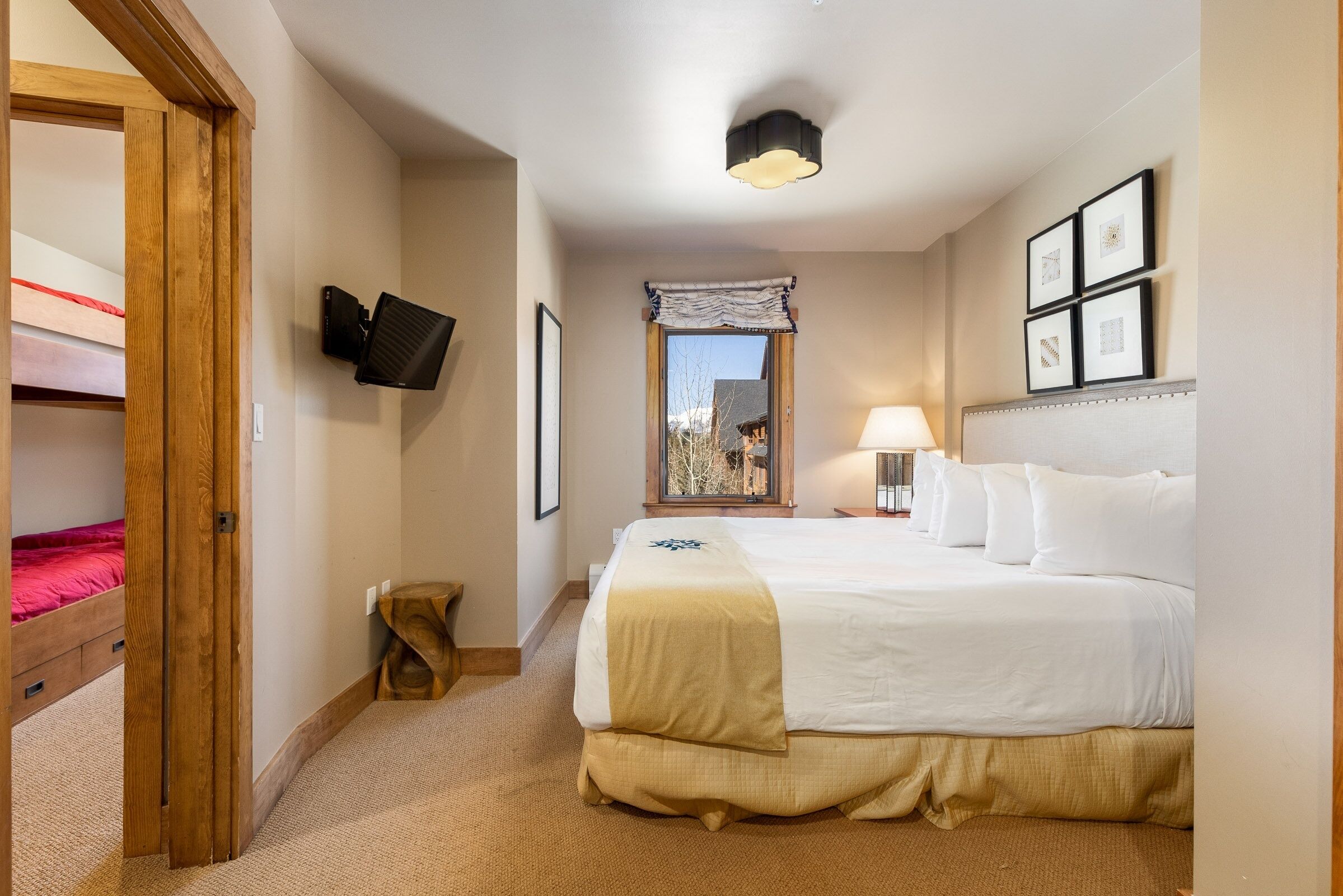 A hotel room with a large bed, a bedside table, a lamp, a TV mounted on the wall, and a window with a view.
