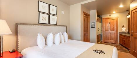 A hotel room with a large bed, a red nightstand, and a wooden wardrobe.