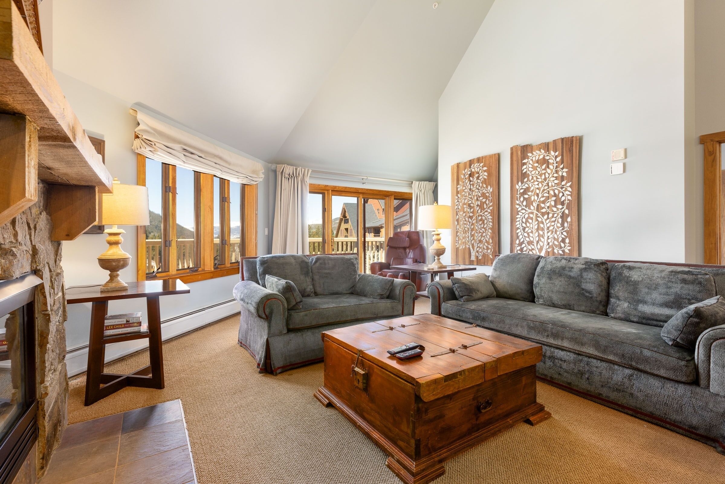 A spacious living room with a high ceiling, large windows, and a fireplace. There are two sofas and a wooden coffee table.