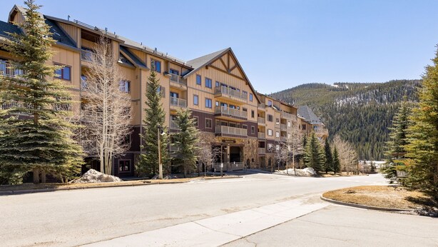 A multi-story hotel with balconies, a stone facade, and a view of a forested mountain.