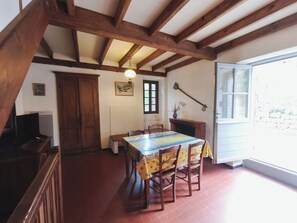 A dining area with a table and chairs, wooden beams on the ceiling, a fireplace, and a window.