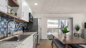 Una cocina moderna con encimera de granito, pileta de acero inoxidable y microondas. Hay una mesa de madera con un banco, y una planta en maceta sobre la mesa.