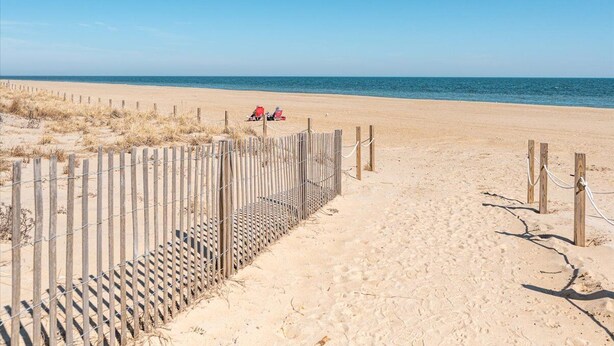 Una playa arenosa con una cerca de madera y una silla roja.