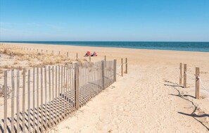 A sandy beach with a wooden fence and a red chair.