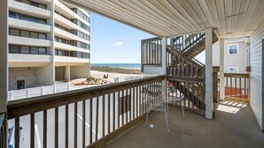 Un balcón con vistas a la playa y un edificio de varios pisos.