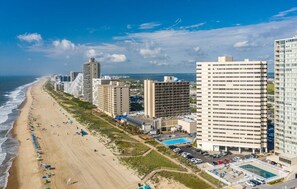Un hotel frente a la playa con varios edificios altos, una playa de arena y una piscina.