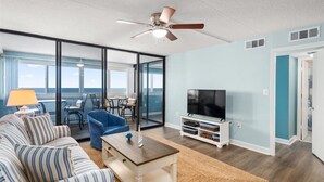 A modern living room with a sofa, blue armchair, and a TV on a white stand. - Gorgeous 2 BR/ 2 BA Beachfront Condo (Ocean City)