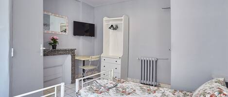 Un dormitorio con cama, cómoda, espejo, televisor y radiador.