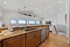 A modern kitchen with granite countertops, wooden cabinets, a dishwasher, and a ceiling fan. - Serendipity | Beachfront | Hot Tub | Golf Cart | Elevator (Anna Maria)