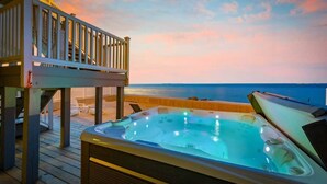 Un jacuzzi en una terraza de madera con vistas al océano al atardecer.
