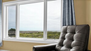 Una habitació amb una finestra gran, una cadira de pell i vistes a una platja i un moll.