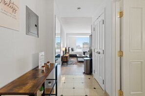 Enter a stylish hallway leading to a bedroom with a dining table, potted plant, and large window offering a city view.