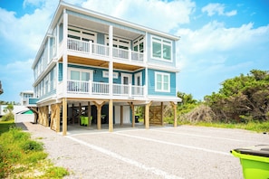 A multi-story beachfront building with balconies, a covered entrance, and a gravel driveway.