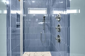A shower with a glass door, a showerhead, and a control panel.
