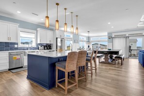 Uma cozinha moderna com uma ilha central, luminárias pendentes e um espaço de jantar com um piano.