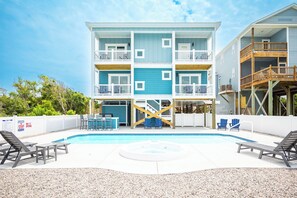 Um edifício com vários andares, piscina, área de estar externa e um deck de madeira.