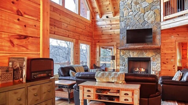 A cozy cabin interior with wooden walls, a stone fireplace, a flat-screen TV, and a leather sofa. - Gated Community, Hot Tub, Game Room (Lake Lure)