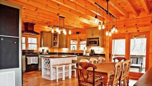 A wooden cabin interior with a kitchen, dining area, and large windows. - Gated Community, Hot Tub, Game Room (Lake Lure)