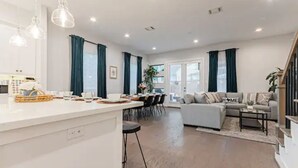 Ein modernes Wohnzimmer mit einer Couch, einem Essbereich mit Tisch und Stühlen sowie einer Küchenzeile mit Arbeitsfläche und Barhockern.