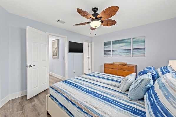 Une chambre à coucher avec un lit, une commode en bois, un ventilateur de plafond et une porte.