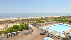 Un espace piscine aménagé sur le toit, avec des chaises longues et des parasols, offrant une vue sur la plage.