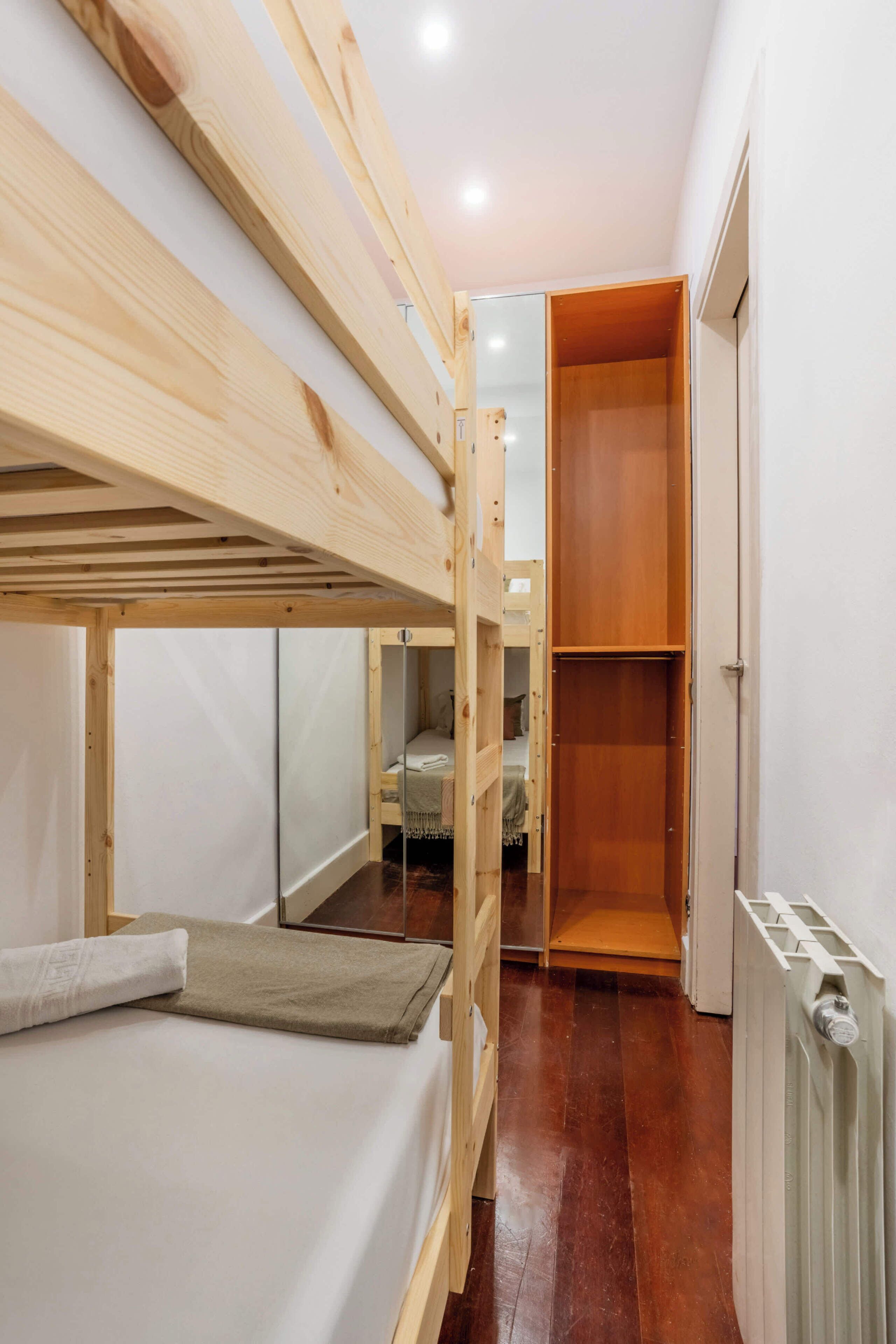 A bunk bed with a wooden headboard, a white mattress, and a beige blanket.