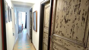 Un couloir avec un sol à motifs, une porte dont la peinture s’écaillait et des tableaux encadrés accrochés aux murs.