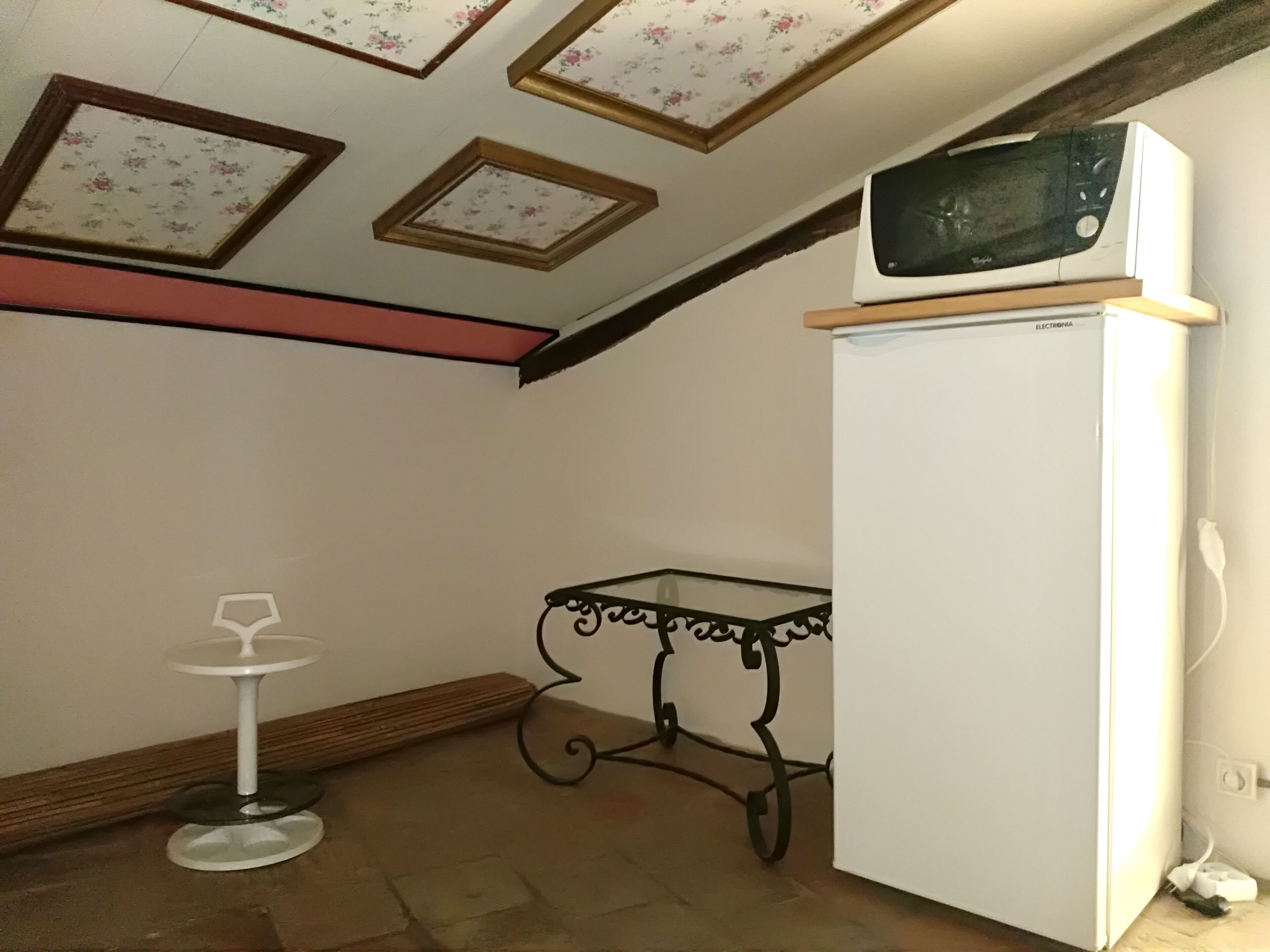 A kitchen with a white refrigerator, a microwave on top, and a small table with a wine glass.
