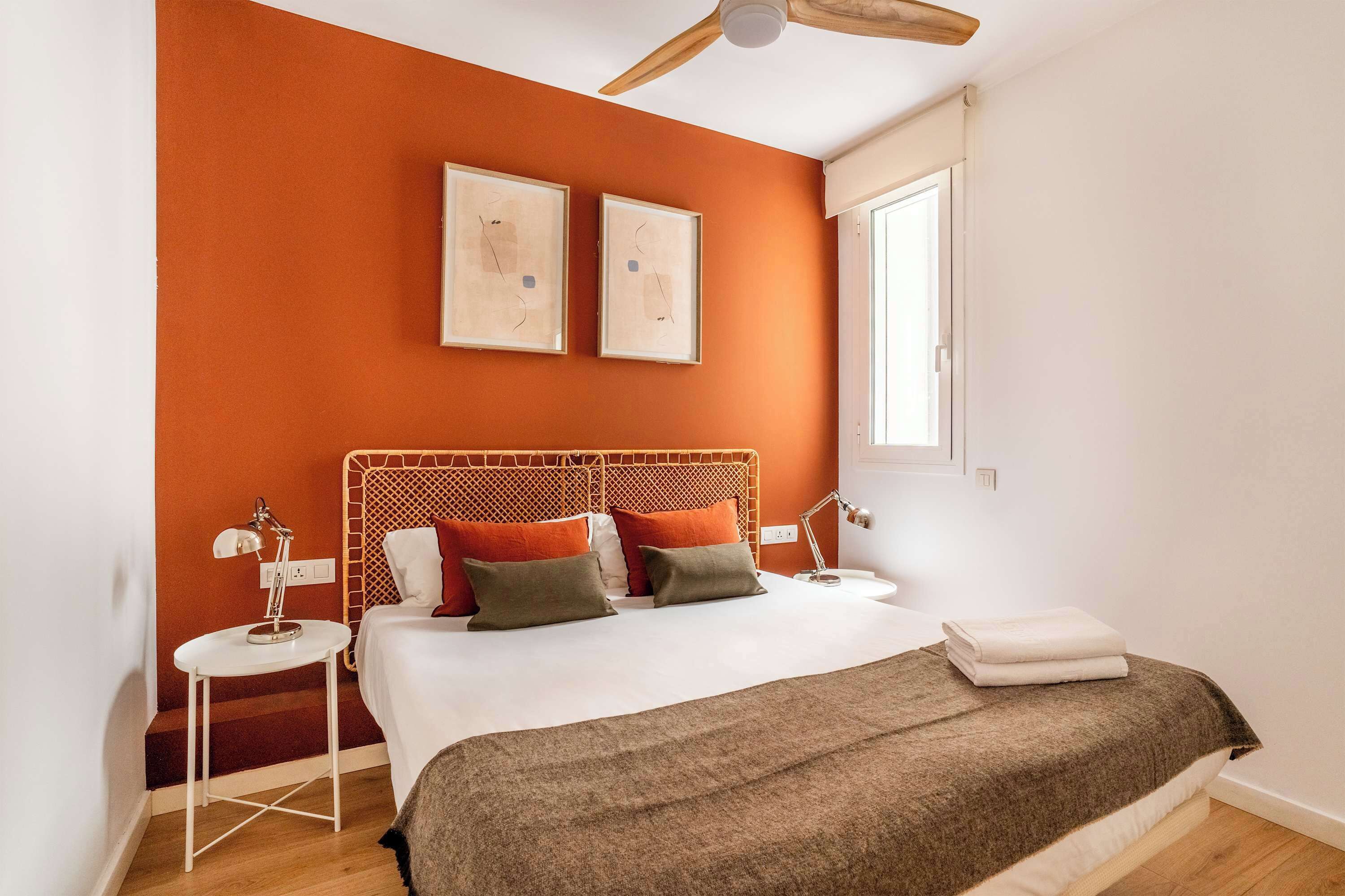A bedroom with a wooden headboard, two bedside tables, a bed with a white and brown blanket, and two framed pictures on the wall.
