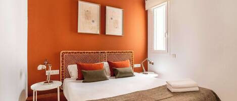 A bedroom with a wooden headboard, two bedside tables, a bed with a white and brown blanket, and two framed pictures on the wall.