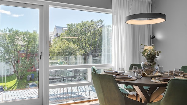 A dining area with a table set for four, a vase with flowers, and a view of a balcony with outdoor furniture. - Luxury's 2 Bedroom Apartment in Downtown Reykjavik with Included parking (Reykjavík)