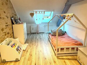 Quarto de criança com beliche, cômoda branca, radiador e janela com cortina.