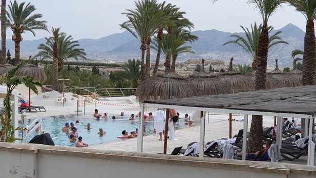 Ein Poolbereich mit Palmen, Liegestühlen und Blick auf die Berge im Hintergrund.