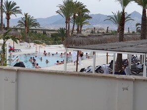 A pool area with palm trees, lounge chairs, and a view of mountains in the background.