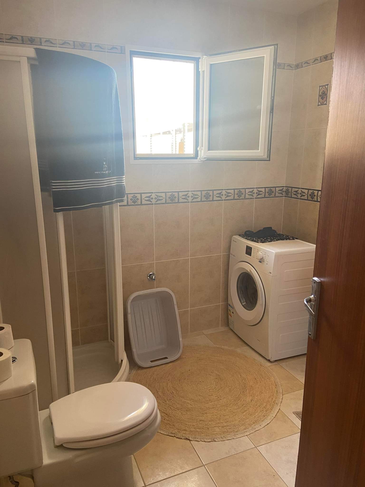 Een kleine badkamer met toilet, wasmachine en douche.