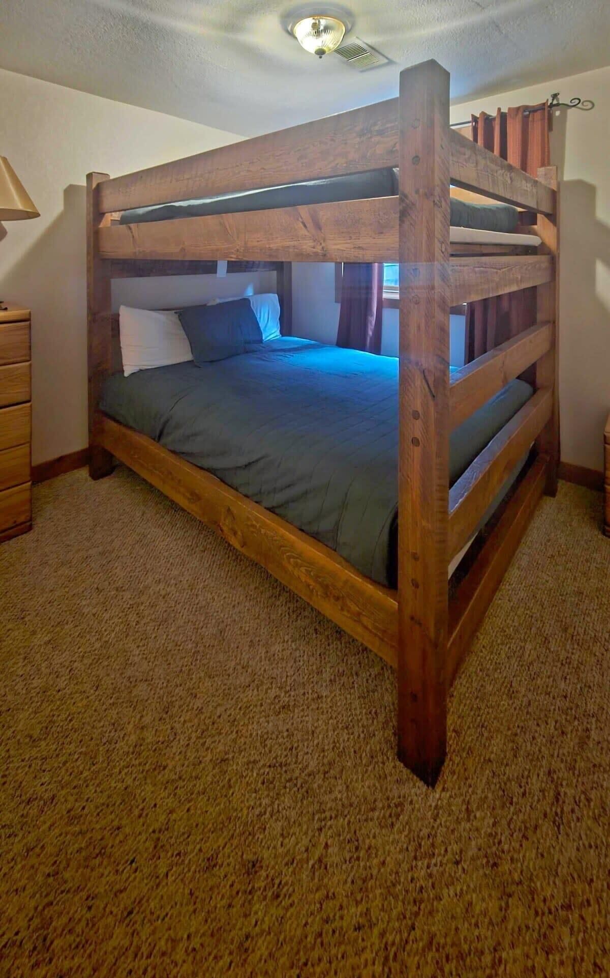 A bunk bed with a wooden frame and a green mattress in a room with beige carpet.