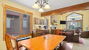 A dining area with a wooden table and chairs, a chandelier, and a view of the outside.