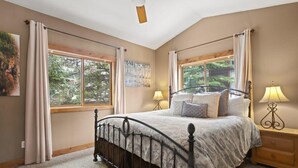 A bedroom with a large bed, two bedside lamps, and a window with curtains.