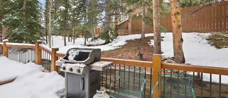 A backyard with a grill, a chair, and a wooden fence.