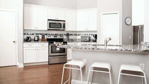 A modern kitchen with white cabinets, stainless steel appliances, a granite countertop, and a bar stool seating area.